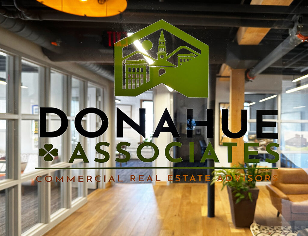 The front door to the Donahue & Associates office; close up on the logo printed on glass with the office visible in the background